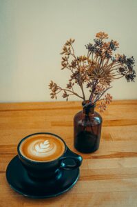 A cozy scene with a latte art coffee and dried flowers on a wooden table.