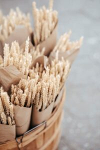 Artisanal dried wheat bouquets wrapped in paper in a rustic wooden basket.