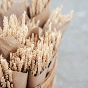 Artisanal dried wheat bouquets wrapped in paper in a rustic wooden basket.